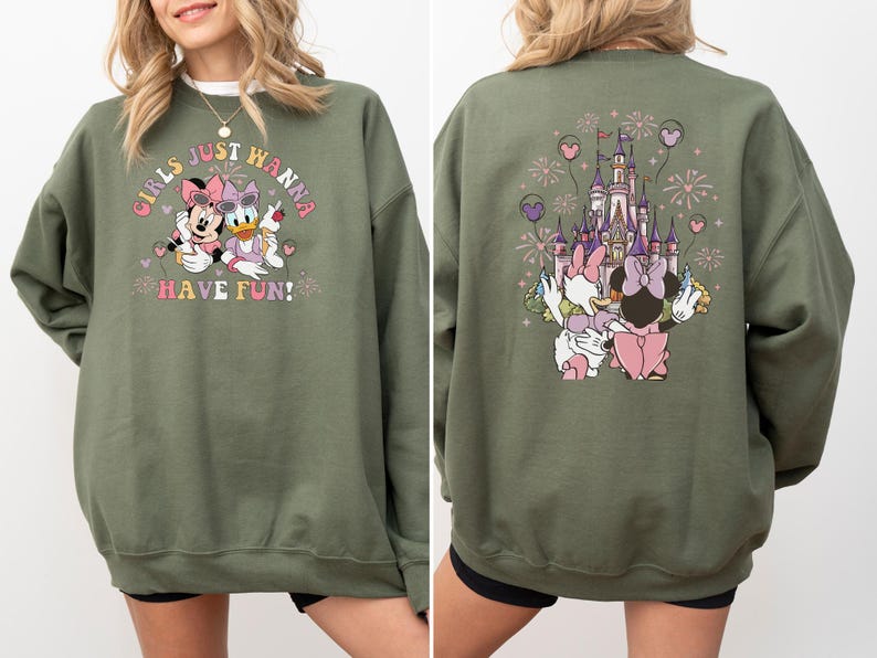 May include: An olive green sweatshirt with a Minnie Mouse and Daisy Duck design and the text "GIRLS JUST WANNA HAVE FUN!". The back features a castle, fireworks, and the two characters. The design is in pink, purple, and white.