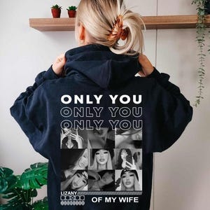Puede incluir: Una sudadera con capucha azul marino oscuro que presenta un estampado gr&aacute;fico blanco en la espalda. El texto ONLY YOU se repite tres veces sobre una cuadr&iacute;cula de nueve fotograf&iacute;as en blanco y negro, con el texto LIZANY OF MY WIFE debajo.