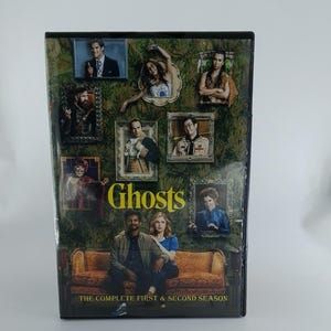 May include: DVD set of the TV show "Ghosts: The Complete First & Second Season." The cover features a collage of character portraits in ornate frames against a green floral wallpaper background. The title "Ghosts" is in yellow.