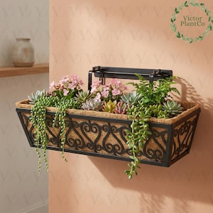May include: A black metal wall-mounted planter box filled with various succulents and pink flowers. The rectangular planter has a decorative scrollwork design and a coir liner. The plants cascade over the sides, creating a vibrant display.