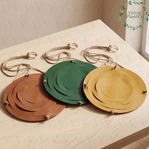 May include: Three circular hanging plant holders in brown, green, and yellow. Each holder consists of concentric circles connected by thin rope, featuring a metal ring at the top for suspension. The design allows for a layered, tiered appearance.