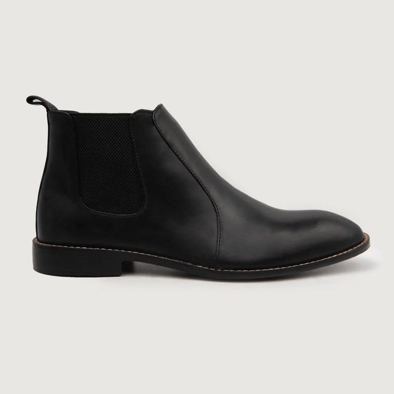 May include: A single black Chelsea boot with a rounded toe and a pull tab at the back. The boot features elastic side panels and a stitched sole. The leather boot is approximately 6 inches tall.
