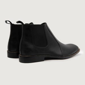 May include: A pair of black leather Chelsea boots. The boots have a rounded toe, elastic side panels, and a pull tab at the back. The soles are a dark brown color with visible stitching. The boots are set against a plain background.