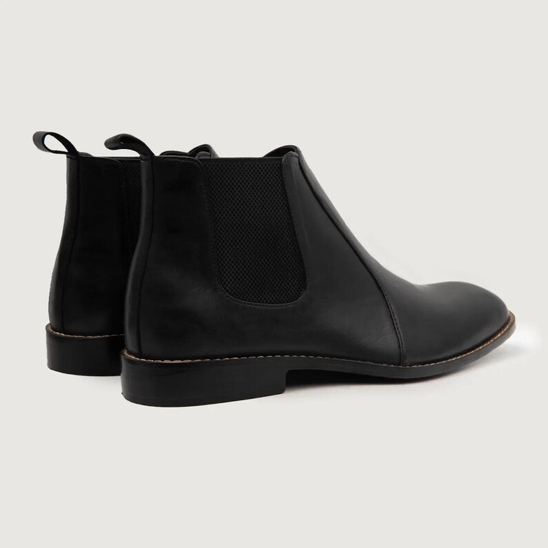 May include: A pair of black leather Chelsea boots. The boots have a rounded toe, elastic side panels, and a pull tab at the back. The soles are a dark brown color with visible stitching. The boots are set against a plain background.