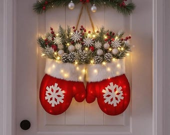 May include: A festive Christmas door decoration featuring two red mitten-shaped ornaments with white snowflake designs. The mittens are adorned with white faux fur trim and illuminated with warm white lights. The top is decorated with pine, berries, and ornaments.