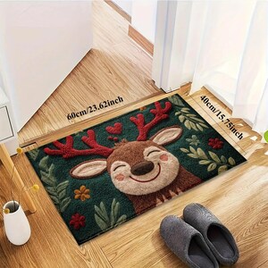 May include: A rectangular doormat featuring a smiling cartoon reindeer with red antlers and a green background. The mat measures 23.62 inches by 15.75 inches and is decorated with hearts and floral accents. A pair of gray slippers rests nearby.