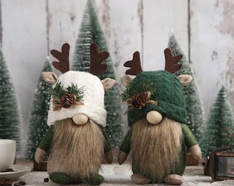 May include: Two Christmas gnomes with brown beards and green and tan bodies. One gnome wears a white knit hat, the other a green knit hat. Both have brown antler accents, pinecone and greenery details, and wooden noses. Decorative holiday figurines.