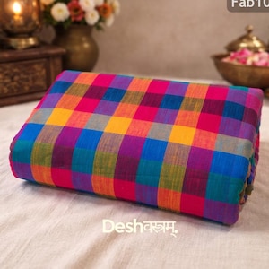 Könnte beinhalten: Ein gefalteter Stoff mit einem lebendigen Karomuster in Pink, Orange, Gelb, Blau und Lila. Der Stoff hat den Text "Fab103" in der oberen rechten Ecke und "Desh वस्त्रम्" unten.