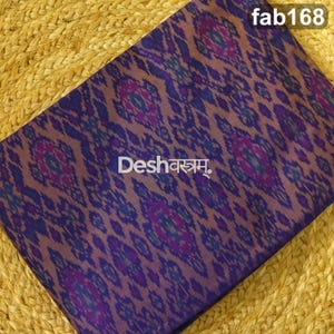 May include: A folded fabric featuring a repeating ikat pattern in shades of purple, blue, and dark brown. The text "fab168" appears in the top right corner, and the text "Deshवस्त्रम्" is printed in white across the center of the fabric.