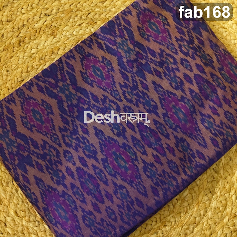 May include: A folded fabric featuring a repeating ikat pattern in shades of purple, blue, and dark brown. The text "fab168" appears in the top right corner, and the text "Deshवस्त्रम्" is printed in white across the center of the fabric.