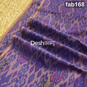 May include: A purple fabric featuring a repeating ikat pattern in shades of dark blue and magenta. The textile displays the text "fab168" in the upper right corner and the text "Deshवस्त्रम्" printed in white across the center of the folds.