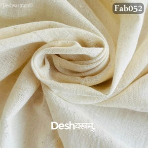 May include: Cream-colored fabric with a woven texture, tightly folded and draped. The fabric has a soft, natural appearance. The text "Fab052" is in the upper right corner. The text "Deshvastram" is in the upper left corner and "Desh वस्त्रम्" is in the lower center.