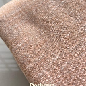 Może przedstawiać: Zbliżenie na złożony kawałek tkaniny w ciepłym, ziemistym odcieniu. Materiał ma teksturowany wygląd z widocznymi nitkami. Tekst "Fab066" znajduje się w białym polu w prawym górnym rogu. Tekst "Deshवस्त्रम" znajduje się na dole.