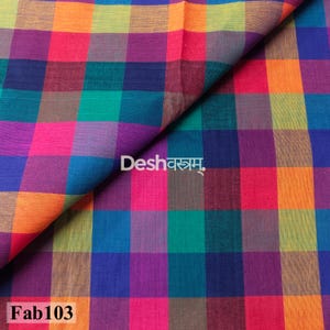 May include: A woven fabric featuring a vibrant multi-colored plaid pattern with squares of orange, yellow, magenta, purple, teal, and blue. The text Deshवस्त्रम् is printed in white in the center, and the text Fab103 is printed in the bottom left corner.