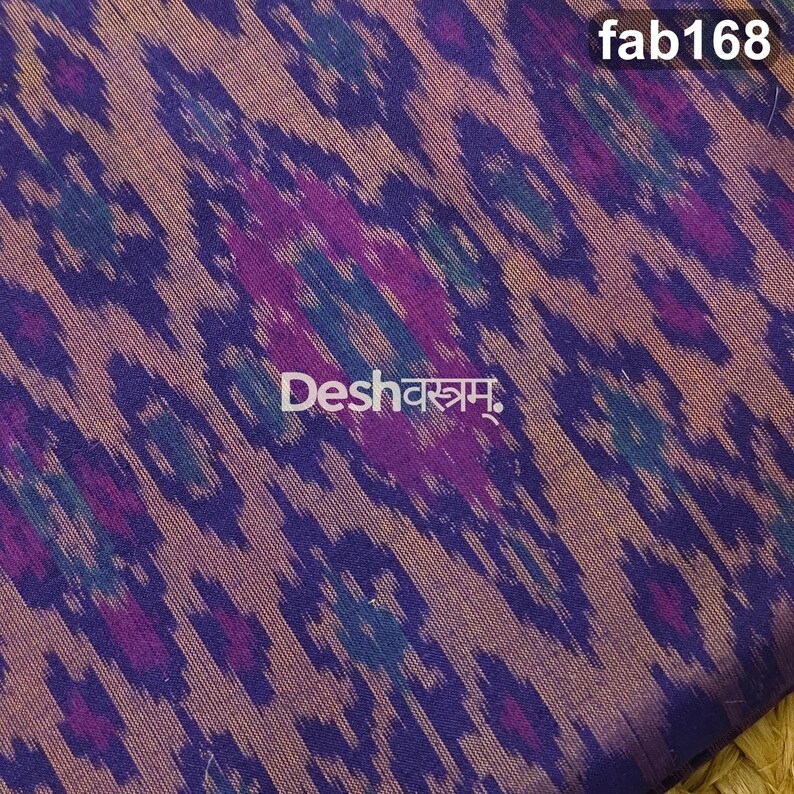 May include: A woven fabric featuring a repeating ikat pattern in shades of deep purple, magenta, and teal against a muted brown background. The text fab168 appears in the top right corner, and the text Deshवस्त्रम् is centered on the fabric.