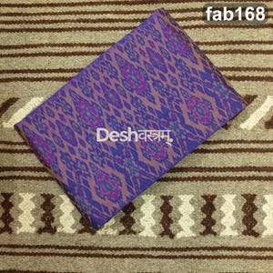May include: A folded piece of fabric featuring a purple and blue ikat pattern with a repeating diamond motif. The text "Deshवस्त्रम्." is printed in white in the center, and the text "fab168" appears in the top right corner of the fabric.