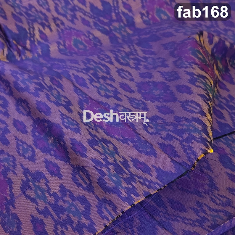 May include: A purple fabric featuring a repeating ikat pattern in shades of blue and violet. The textile displays the text fab168 in the top right corner and the word Deshवस्त्रम् in the center, printed in a clear white font on the surface.