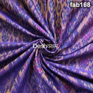 May include: A purple and tan fabric featuring an ikat pattern with a swirling center. The text 'fab168' appears in the top right corner, and the text 'Deshवस्त्रम्' is printed in the center of the fabric with a woven texture.