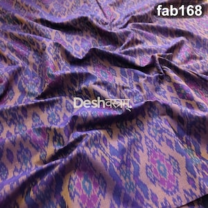 May include: A fabric featuring a purple and brown ikat pattern with repeating diamond-like motifs. The textile displays a soft, draped texture with the text fab168 in the top right corner and the text Deshवस्त्रम् in the center.