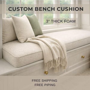 May include: A custom bench cushion with 3 inch thick foam, featuring a light beige textured fabric. The cushion is topped with a matching beige throw blanket with fringe, a beige throw pillow, and a sage green throw pillow on a bench.