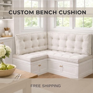 May include: A custom bench cushion in a kitchen setting. The off-white cushions are button-tufted and sit atop a white bench with gold-coloured hardware. The text "CUSTOM BENCH CUSHION" is displayed at the top.