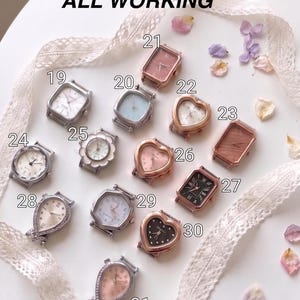 May include: A collection of thirteen assorted wristwatch cases labeled 19 through 31, featuring various shapes including heart, rectangular, and octagonal designs in silver, gold, and rose gold tones, with the text ALL WORKING displayed above.