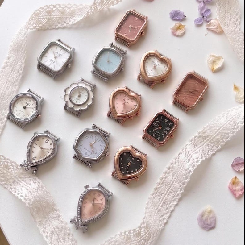 May include: A collection of twelve assorted wristwatch cases in various shapes including rectangular, heart, circular, and teardrop designs. The cases feature metallic finishes in silver, gold, and rose gold tones with diverse dial colors and markers.