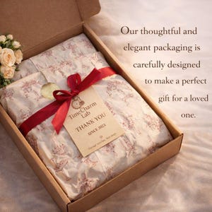 May include: A brown cardboard box with a red ribbon and a tag that reads "TimeCharm Lab THANK YOU SINCE 2023." The box contains tissue paper with a red pattern. The text on the right says "Our thoughtful and elegant packaging is carefully designed to make a perfect gift for a loved one."