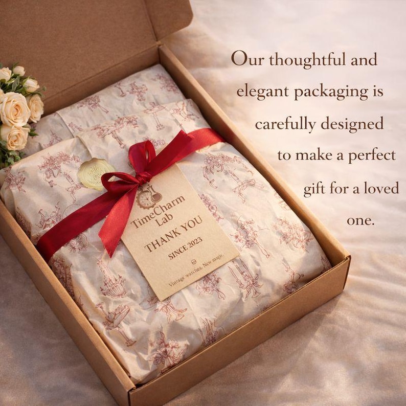 May include: A brown cardboard box with a red ribbon and a tag that reads "TimeCharm Lab THANK YOU SINCE 2023." The box contains tissue paper with a red pattern. The text on the right says "Our thoughtful and elegant packaging is carefully designed to make a perfect gift for a loved one."