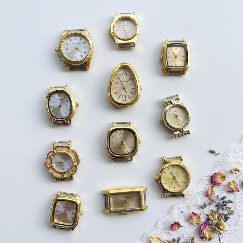 May include: A collection of eleven gold-tone watch heads in various shapes including round, square, rectangular, and teardrop. Each watch face features gold or silver dials with hour markers and hands, presented without straps on a plain white surface.