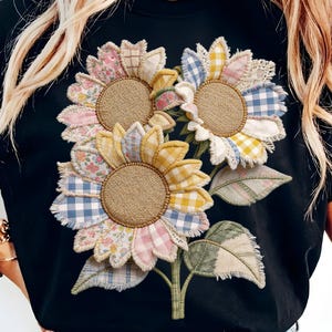 Pode incluir: Camiseta preta com um design de aplicação de três girassóis. Os girassóis têm centros de juta e pétalas com vários padrões pastel, incluindo florais, xadrez e cores sólidas. Folhas e caules verdes completam o design.