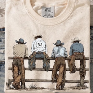 Könnte beinhalten: Cremefarbenes Sweatshirt mit einer Grafik von vier Cowboys, die sich an einem Holzzaun anlehnen. Die Cowboys tragen Hüte, Chaps und Stiefel. Ein Cowboy hat die Nummer 940 auf dem Rücken. Das Shirt hat ein Comfort Colors-Etikett.
