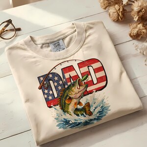 Close-up of a patriotic fishing dad shirt design showing detailed largemouth bass leaping from splashing water with American flag stars and stripes inside DAD text, a perfect Father's Day digital download