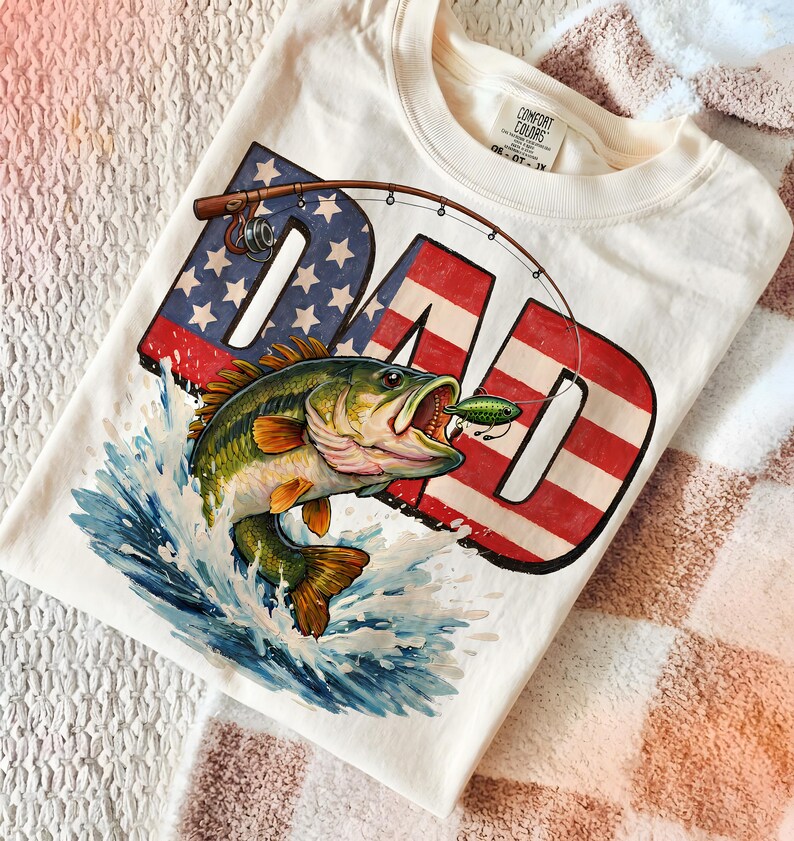 Black shirt mockup with a bold patriotic fishing dad PNG design showing a largemouth bass biting a lure over American flag DAD lettering, great for outdoor dad and fisherman apparel
