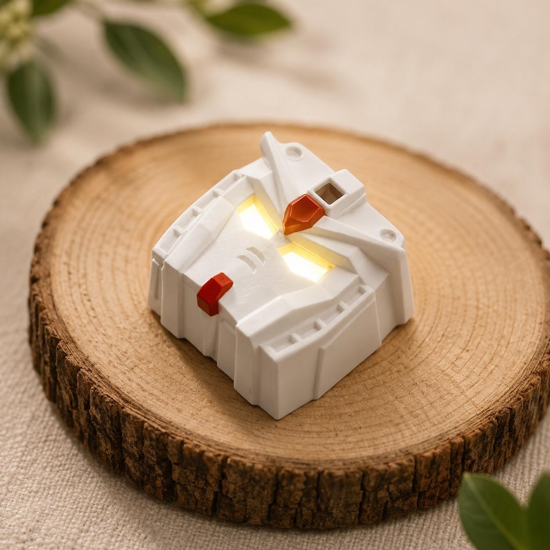 May include: A white mechanical robot head keycap featuring a geometric design with a red chin accent and a metallic copper-colored forehead crest. The eyes are illuminated with a bright yellow light, creating a glowing effect on the white surface.