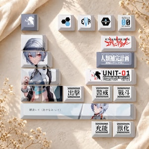 May include: A set of white and grey mechanical keyboard keycaps featuring anime character illustrations, NERV logos, and Japanese text including 'UNIT-01', 'EVANGELION', 'SEELE', and various kanji characters like '出撃', '警戒', '戦闘', '充能', '獸化', and '人類補完計画'.