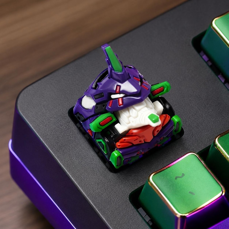 May include: A custom mechanical keyboard keycap shaped like a stylized robot head. The keycap features a purple, green, white, and red color scheme with intricate mechanical detailing, including a pointed crest and a white faceplate design.