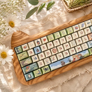 May include: A mechanical keyboard with a wooden case shaped like cat ears. The keycaps are cream-colored with dark brown letters and feature various colorful illustrations of animated characters, including a black cat and a castle, across the keys.