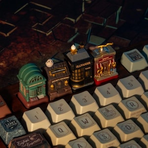 Puede incluir: Figuras en miniatura de tiendas de una serie de fantasía, incluyendo la tienda de varitas de Ollivander, sobre un teclado. Las figuras están detalladas con varios colores y diseños arquitectónicos. Las teclas del teclado son beige con letras negras.