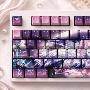 May include: A white mechanical keyboard featuring custom keycaps in shades of purple and pink. The keys display anime-style illustrations, star motifs, and the text Aemeath. The layout includes standard function keys and alphanumeric characters.