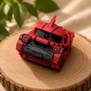May include: A red and black mechanical robot figurine featuring a rounded head with a single central eye, a prominent antenna, and a textured, blocky chassis. The design includes black panel lines and a thick, segmented tube wrapping around the head.