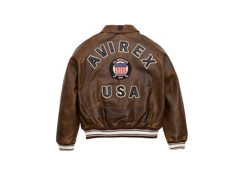 Pu&ograve; includere: Giacca in pelle marrone con la scritta "AVIREX" ad arco sulle spalle e "USA" sotto. Una toppa circolare con la bandiera americana &egrave; centrata tra le parole. La giacca ha una fascia a righe bianche e marroni in vita e sui polsini.