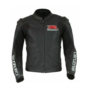 Puede incluir: Chaqueta de moto negra con el logo de Suzuki en rojo y blanco. La chaqueta tiene cuello alzado, hombros acolchados y la palabra "SUZUKI" impresa en blanco en las mangas. La chaqueta está hecha de un material duradero.