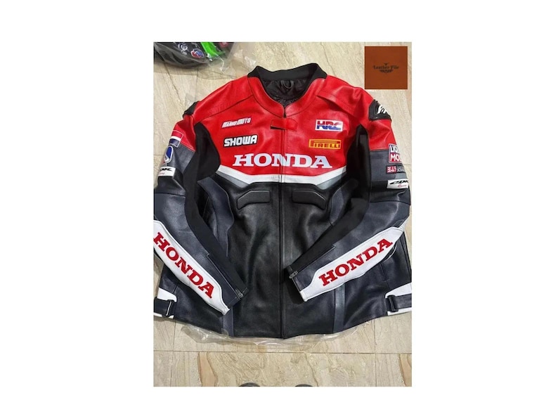 May include: A black, red, and white Honda motorcycle racing jacket. The jacket features the Honda logo, along with sponsor logos like Showa and Pirelli. The jacket has a stand-up collar and a zipper closure.