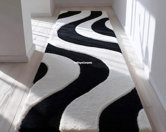Puede incluir: Una alfombra pasillera rectangular con textura de pelo largo y un patrón ondulado en blanco y negro. El diseño consiste en franjas curvas y fluidas que recorren toda la longitud de la alfombra. El texto SabhyaCarpets es visible.