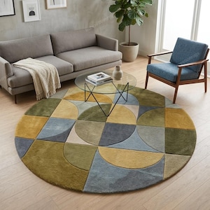 May include: A circular rug with a geometric pattern in a living room setting. The rug's design incorporates squares and semi-circles in green, yellow, blue, and beige. It's placed on a wooden floor, with a sofa, chair, and coffee table visible.