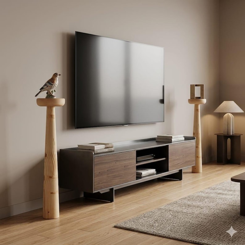 May include: A modern living room setup featuring a large flat-screen TV mounted on a neutral-colored wall. A wooden TV stand with storage sits below the TV. Decorative wooden pedestals with bird and geometric accents flank the TV.