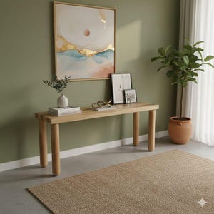 Puede incluir: Una consola de madera de color claro con cuatro patas redondeadas. La mesa está adornada con objetos decorativos, que incluyen arte enmarcado, libros y una escultura dorada. Una gran pintura abstracta cuelga de la pared sobre la mesa y una planta en maceta está cerca.