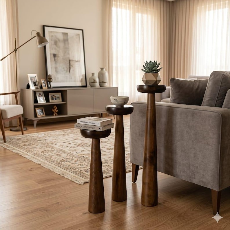 May include: Three wooden side tables of varying heights with a dark finish. The tables have a round top and a conical base. One table holds a small succulent in a geometric pot. The tables are in a living room setting.