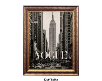 May include: A framed black and white photograph of a New York City street scene featuring the Empire State Building centered in the distance. The word VOGUE is printed in large white capital letters over the image. The frame is ornate and dark gold.